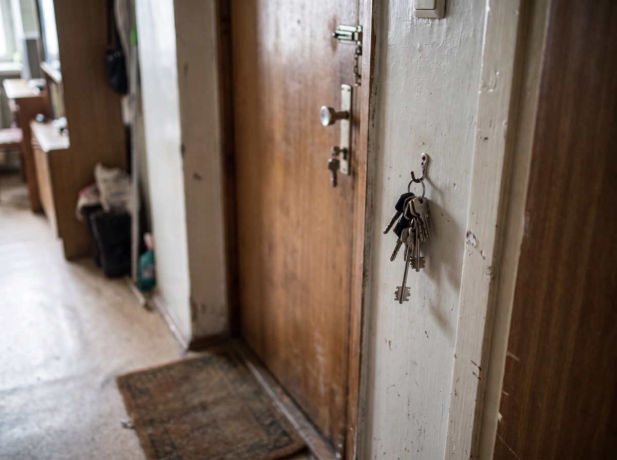 The inside of a modest apartment front door with keys hanging on a hook beside it.
