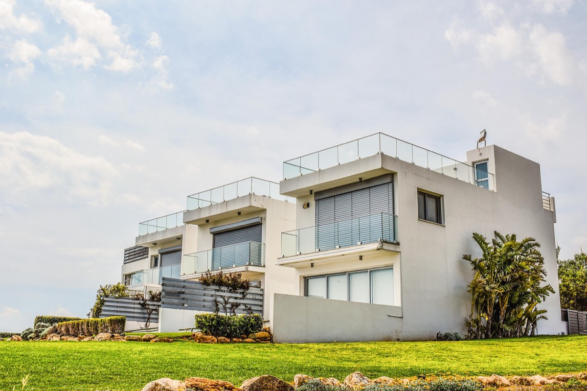 A modern white home with clean lines set on a green rise under an open sky.
