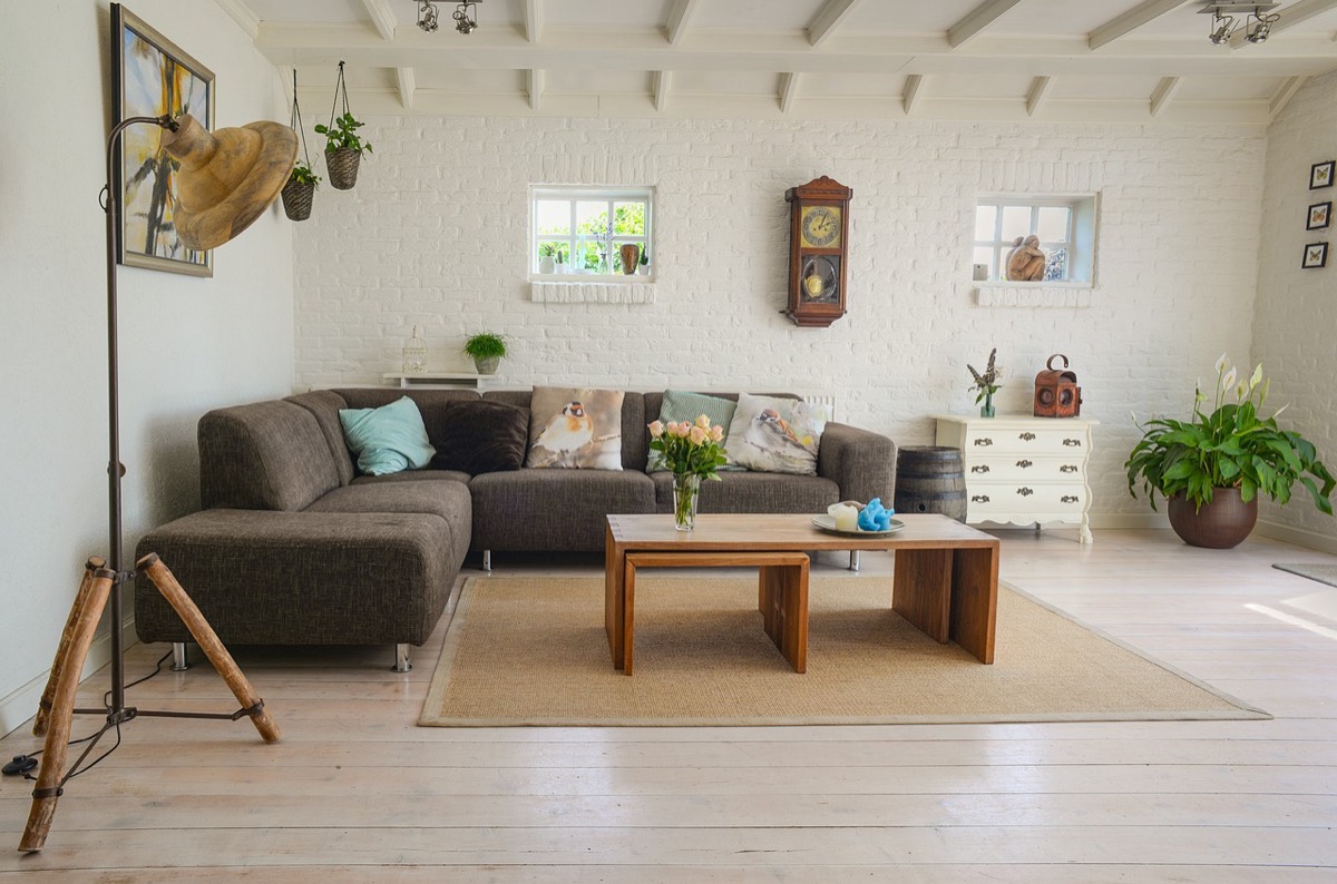A light-filled living room with a white brick wall, a low wood table, and green plants.