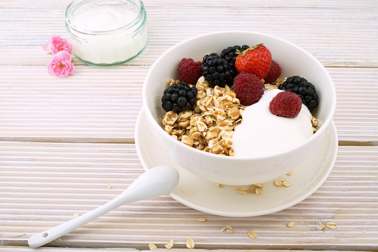 A white bowl of granola with yogurt and a pile of fresh berries.