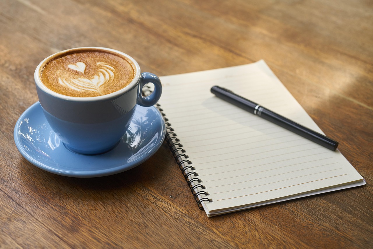 A latte with leaf art in a ceramic cup on a wooden table.