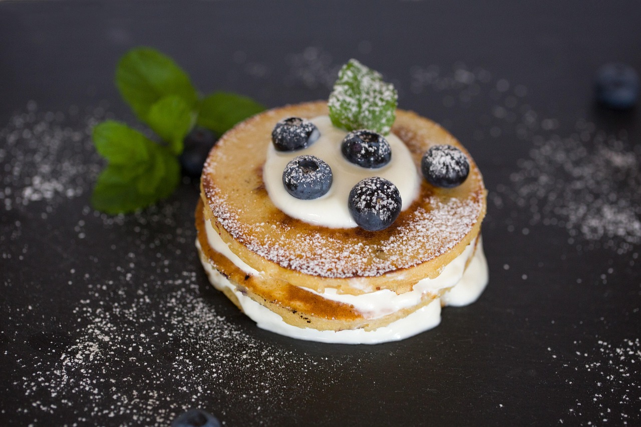 A stack of golden pancakes topped with blueberries, cream, and powdered sugar.